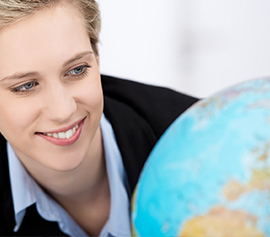 Eine Geschäftsfrau mit einem schwarzen Blaser, lächelt und schaut auf einen Globus.
